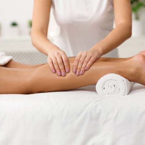 Massage therapist massaging woman calves in spa center, side view